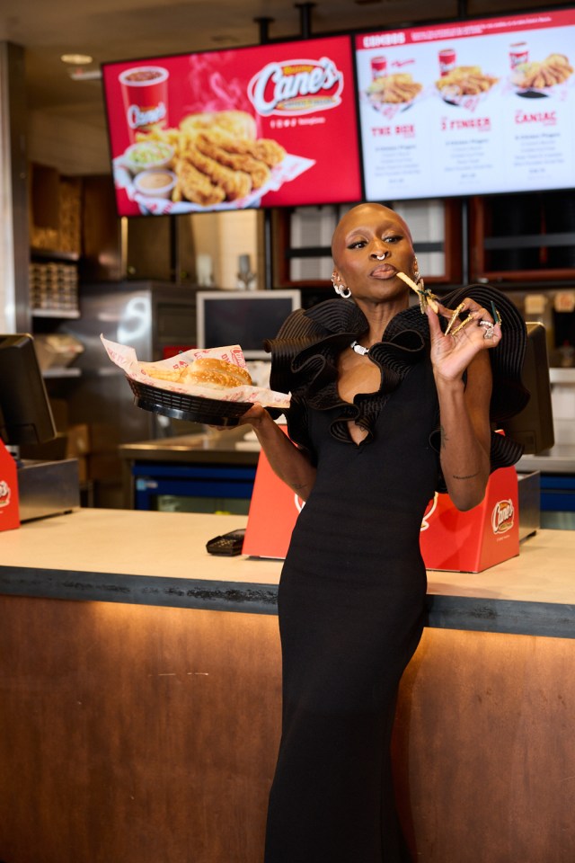 A person in a black dress holding Raising Cane's food in a UK restaurant.