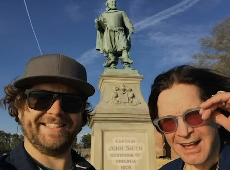 Photo of two men smiling in front of a statue of Captain John Smith.