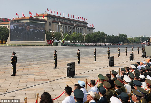 A screen shows Chinese President Xi Jinping as he stands in a car to review the troops during a military parade