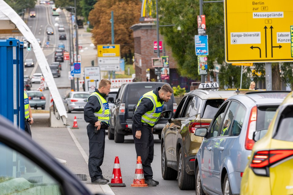 German police officers checking cars at a border crossing.