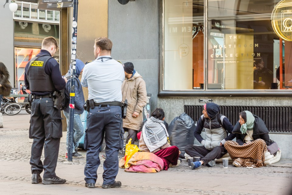 Police officers checking the documents of immigrants sitting on the street.