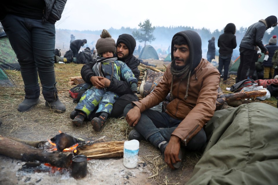 Migrants warming themselves by a bonfire at a border camp.