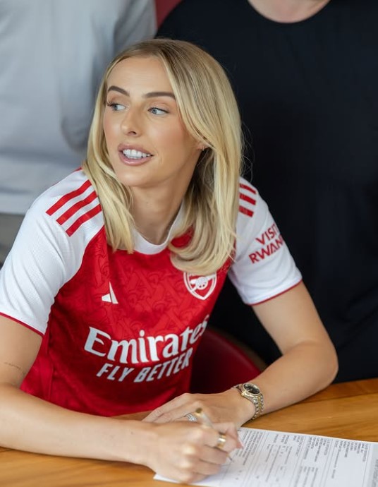 Woman in Arsenal jersey signing a document.