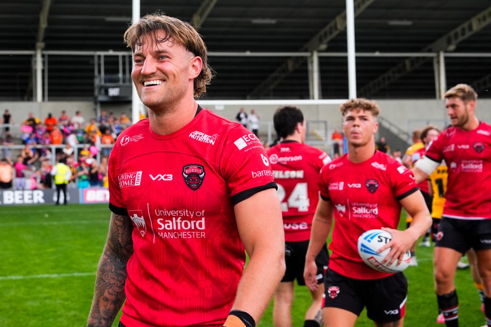 A smiling Salford Red Devils rugby player in a red jersey.