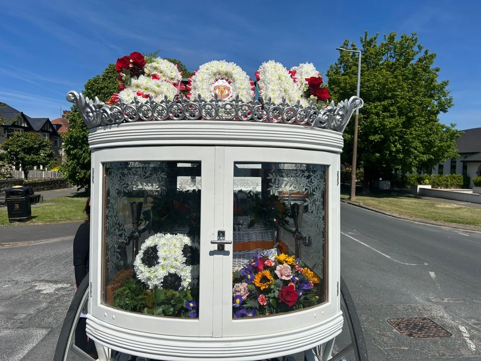 Hearse decorated with floral tributes, including a Manchester United emblem.