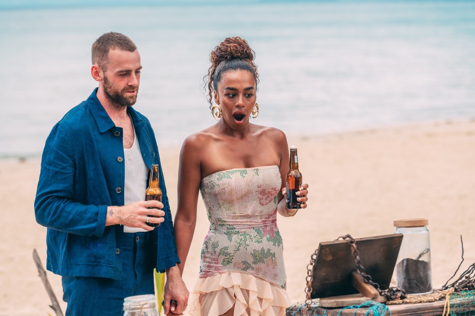 A man and woman on a beach, holding beers, looking surprised.