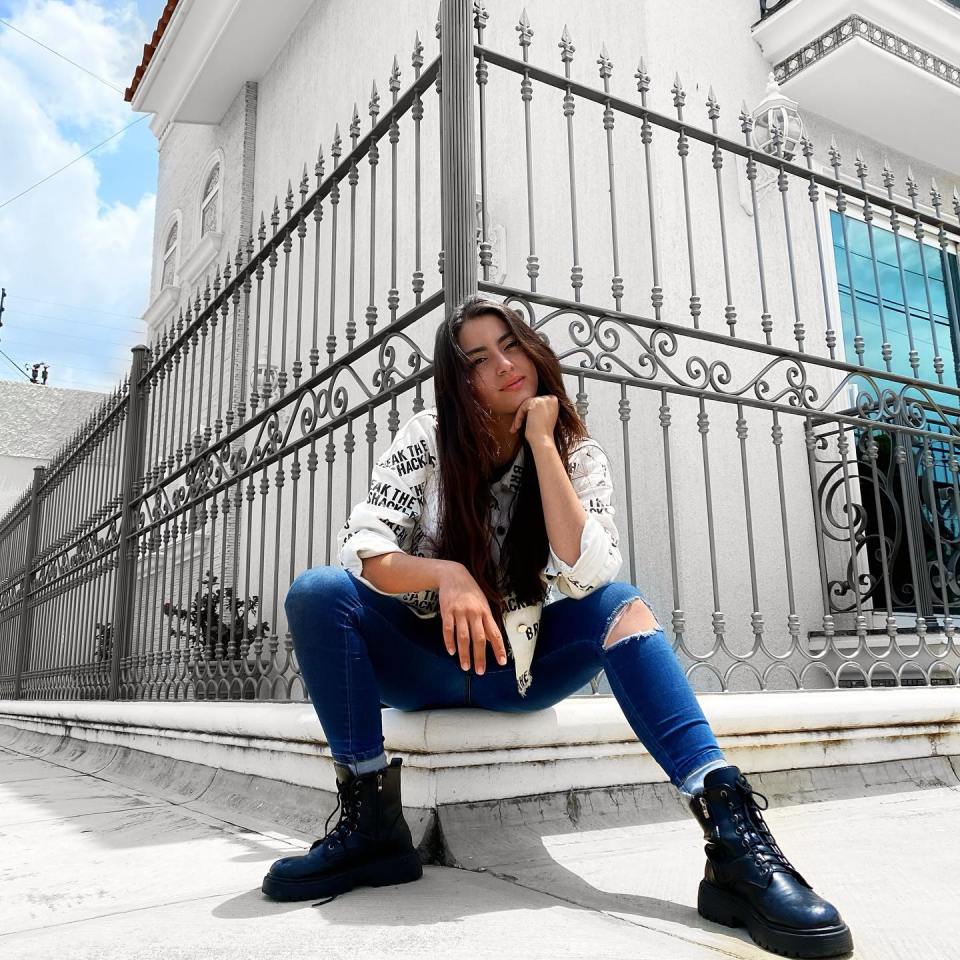 A young woman sits in front of an ornate metal fence.