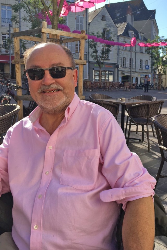 Steve Holbrook-Sishton, wearing a pink shirt and sunglasses, sits at an outdoor cafe.