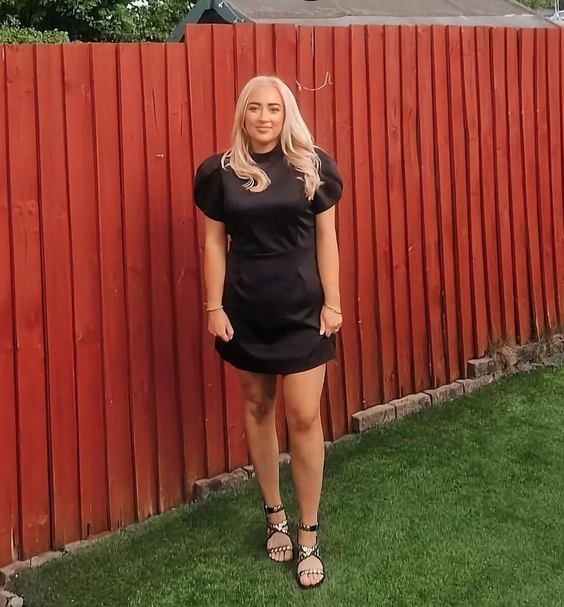 Woman in black dress in front of a red fence.  Text overlay: "You will lose a shit load of weight!"