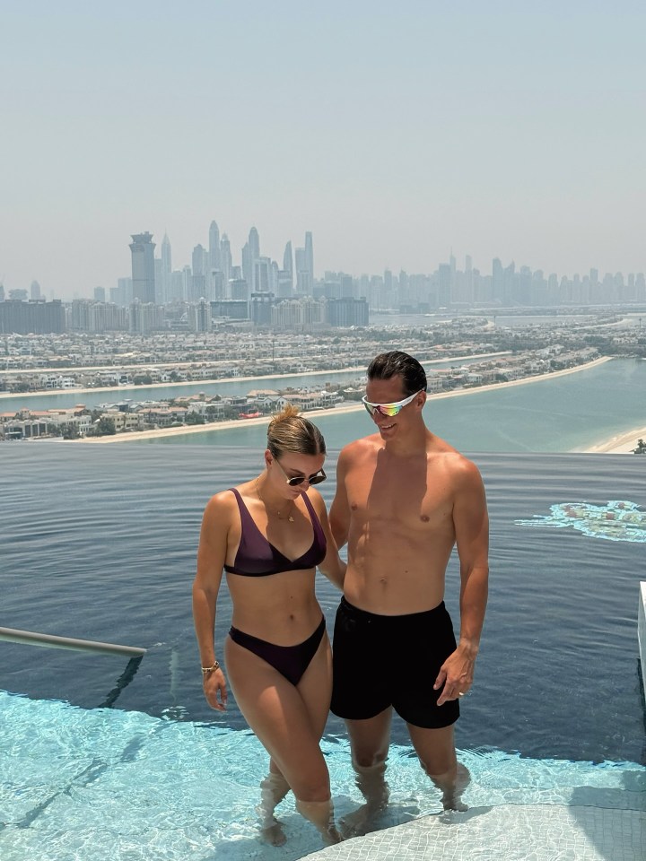 Couple in swimwear in infinity pool overlooking Dubai skyline.