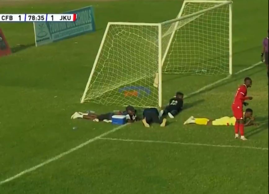 Soccer players lying on the ground during a match interruption caused by a swarm of bees.