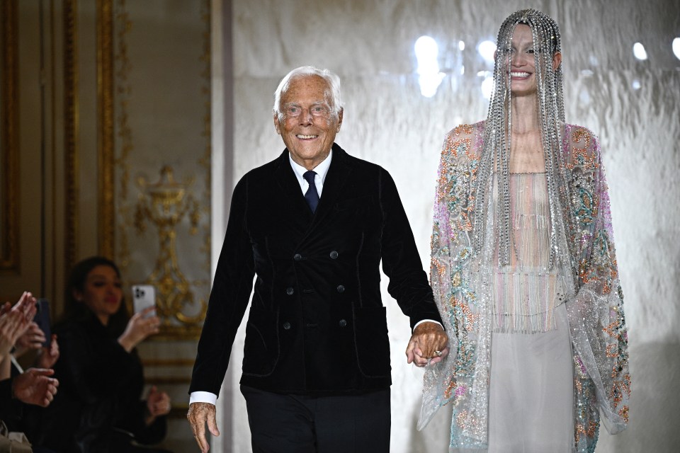 Giorgio Armani and a model holding hands at a fashion show.
