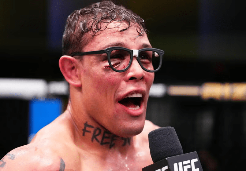 Injured fighter with "Free" tattooed on his neck speaks into a microphone.
