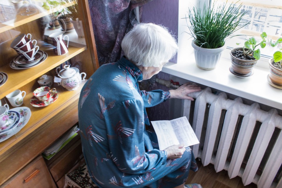 Senior woman reviewing a gas bill while touching a radiator.