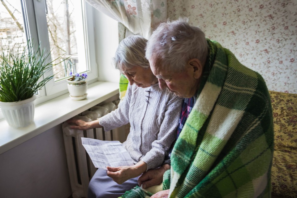 Senior couple reviewing a gas bill while wrapped in a blanket near a radiator.