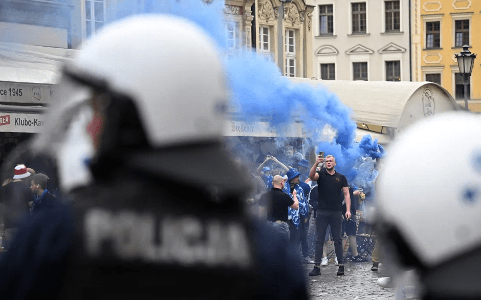 Police officers watching soccer fans with blue smoke bombs.