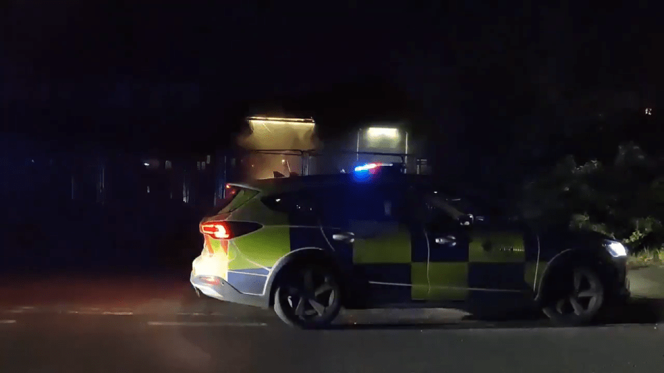 Police car at night near a building where flares were reportedly thrown.