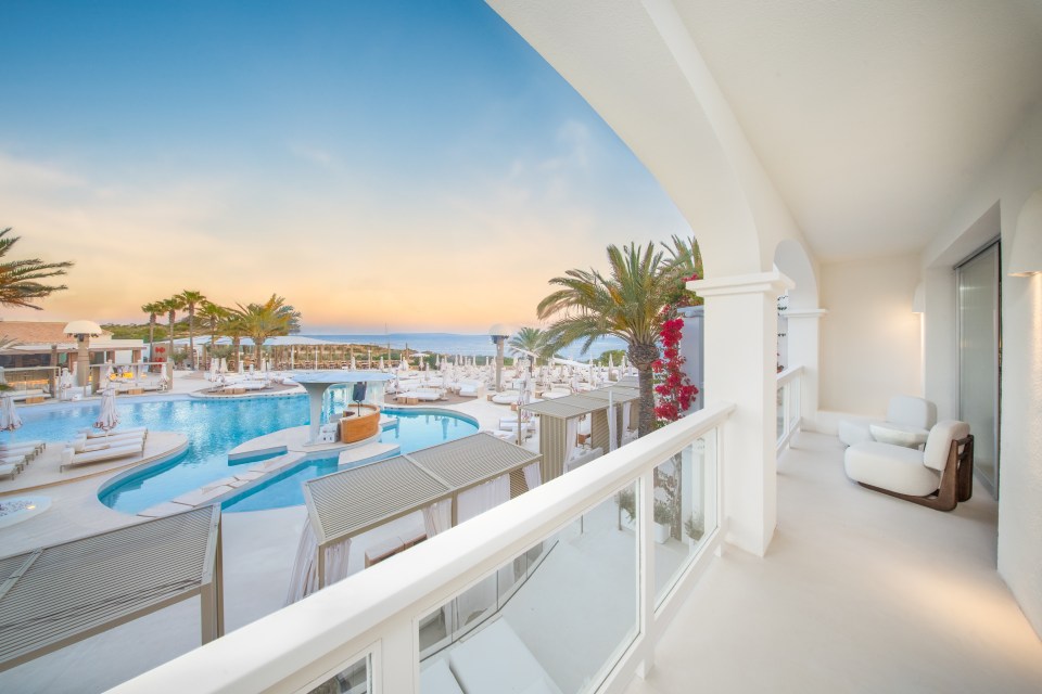Balcony view of a resort pool and ocean at sunset.