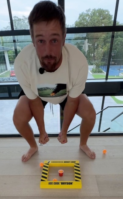 Man playing a game, aiming ping pong balls into a cup.