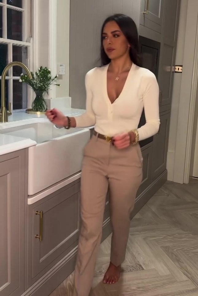 Woman in a cream sweater and beige pants in a kitchen.
