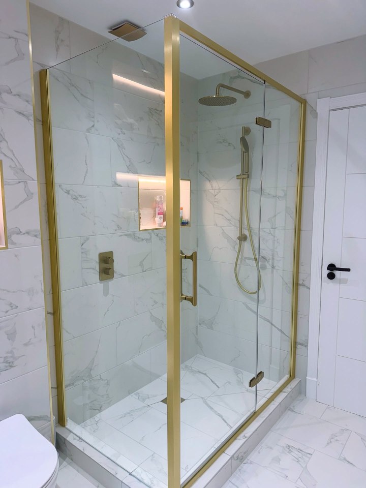 Gold-framed glass shower enclosure in a marble-tiled bathroom.