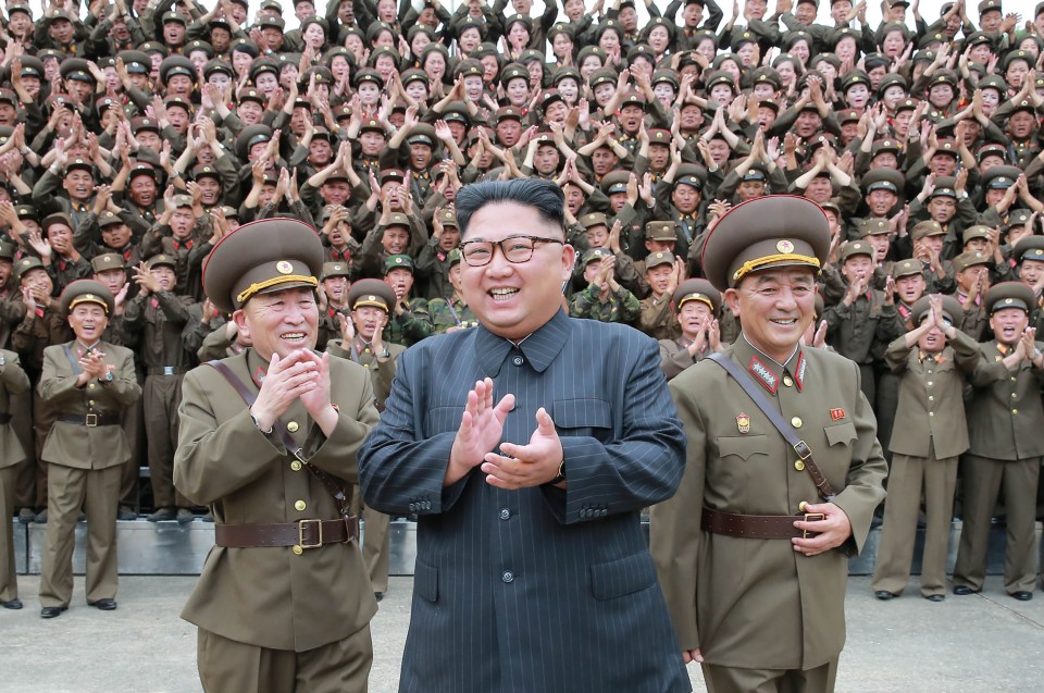Kim Jong-Un and military officials applaud before a large crowd.
