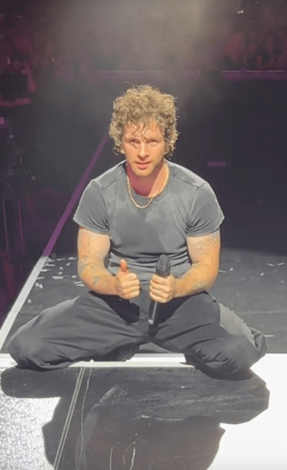 Performer kneeling on stage, holding a microphone and giving a thumbs up.