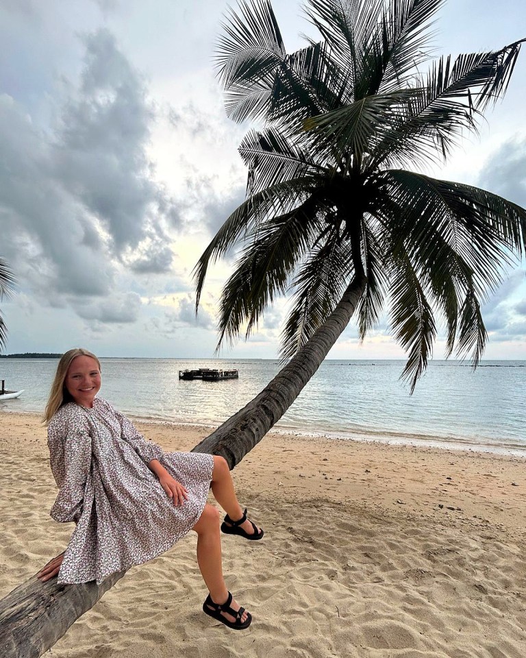 Woman sitting on a palm tree trunk on a beach.