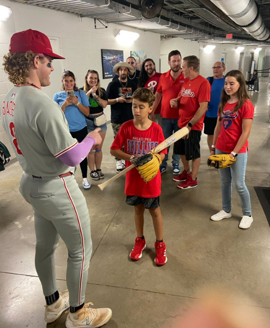 A baseball player talking to a young boy holding a bat, surrounded by other people.