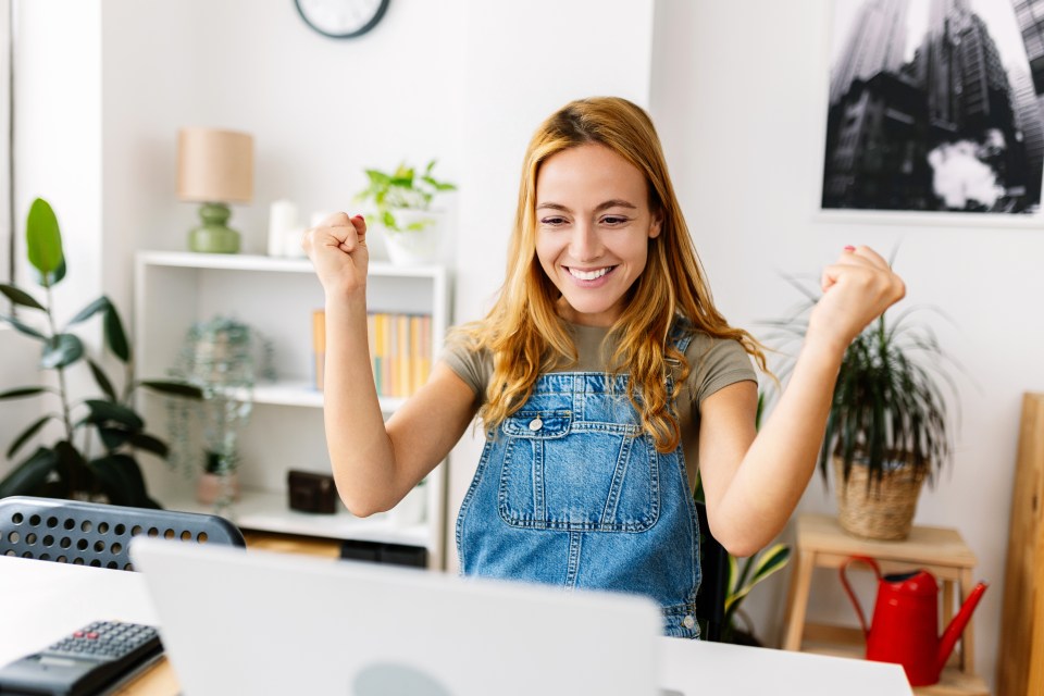 A cheerful woman celebrates a success on her laptop.