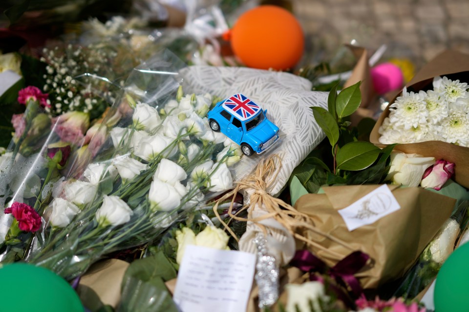 Toy car with UK flag among flowers at a memorial.
