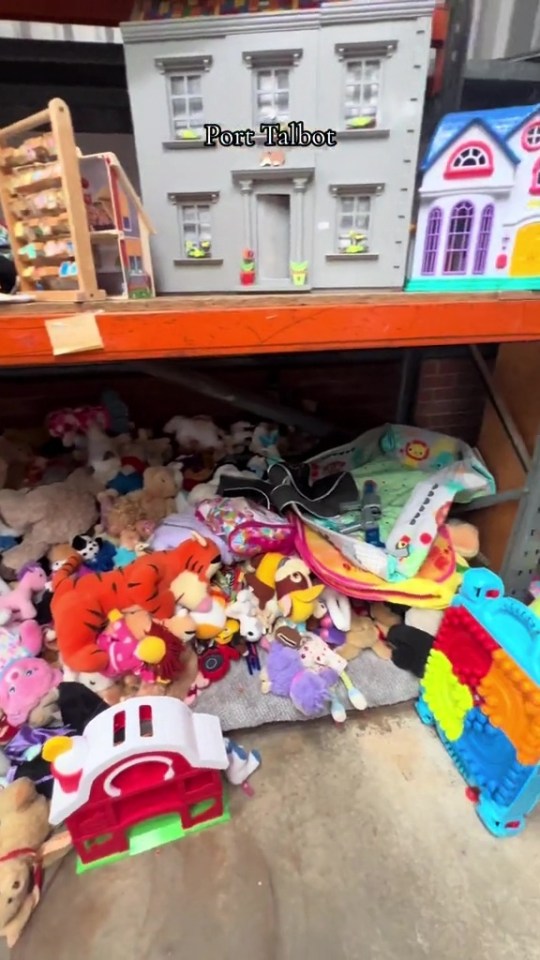 A shelf of toys, including dolls' houses and a large pile of stuffed animals.