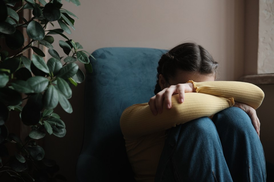 Teenage girl sitting and crying, covering her face with her hands.