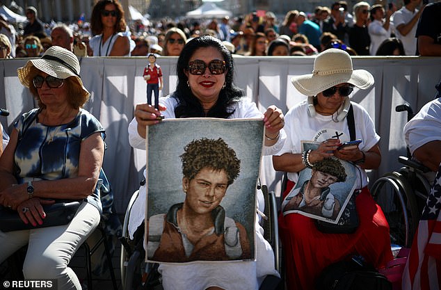 A woman holds a figure and a tapestry depicting Carlo Acutis on the day Pope Leo XIV leads a Holy Mass for the canonisation of the 15-year-old, in St. Peter's Square at the Vatican