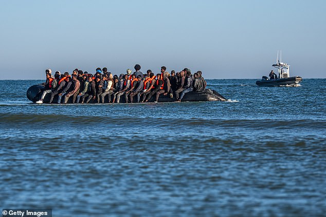 A French police vessel looks on as a dinghy laden with people prepares to cross the English Channel near Gravelines, northern France