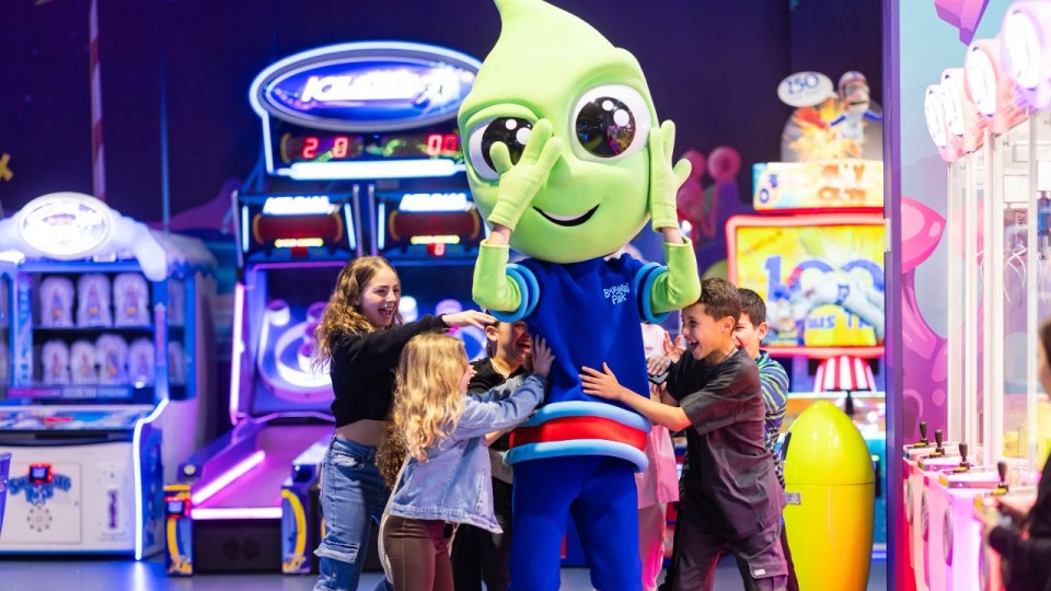 Children surrounding a mascot at an arcade.