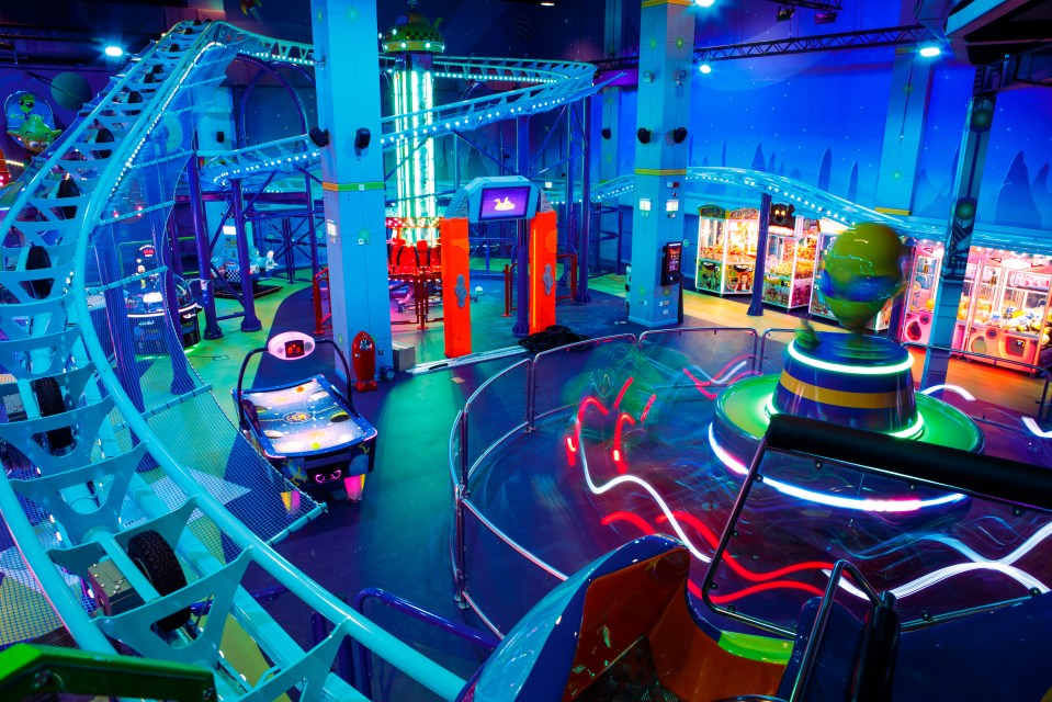 Interior view of Babylon Amusement Park in London, showing a roller coaster, a spinning ride, and arcade games.