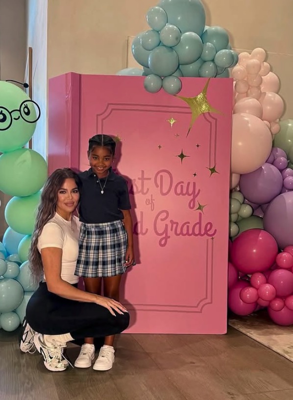 Khloe Kardashian and her daughter posing in front of a "Last Day of 1st Grade" backdrop.