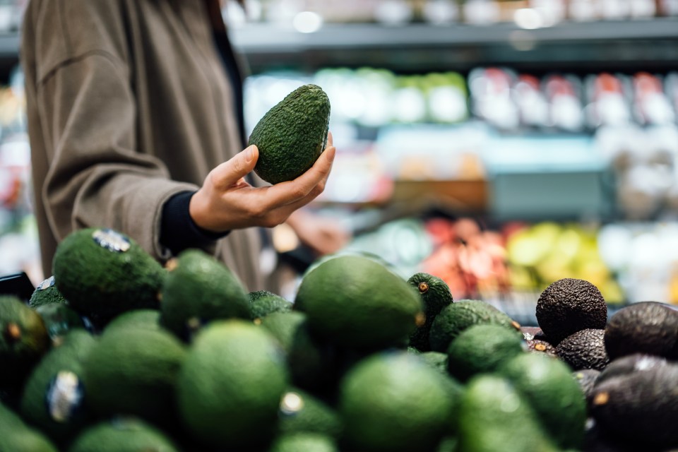 Woman's hand selecting an avocado from a display of avocados at a grocery store.