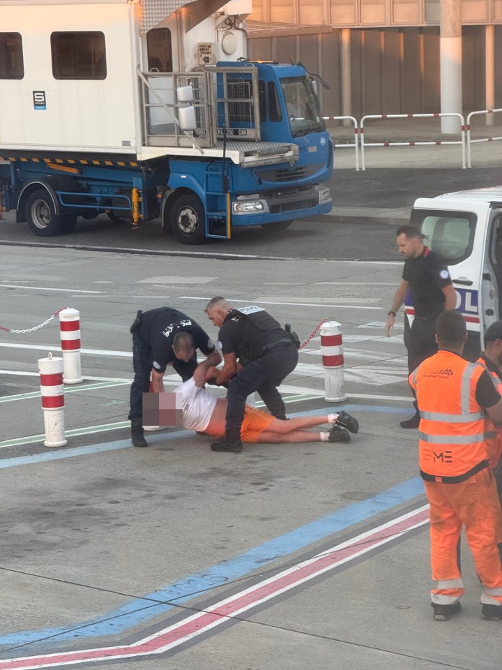Police officers arresting a man on an airport tarmac.