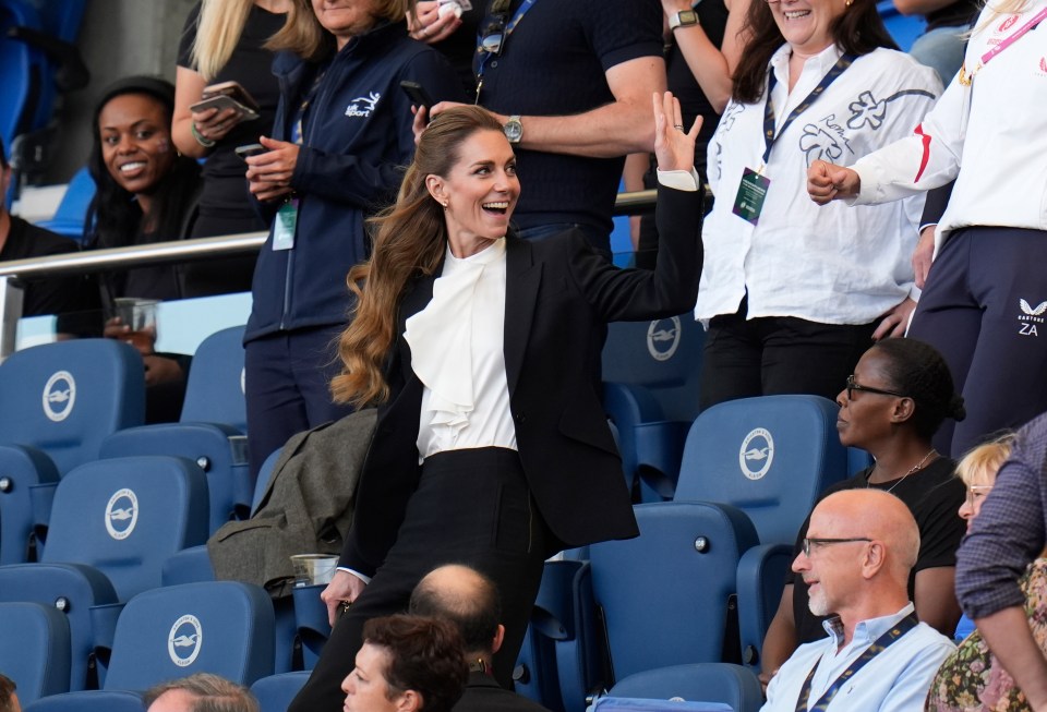 The Princess of Wales waves from the stands at a rugby match.