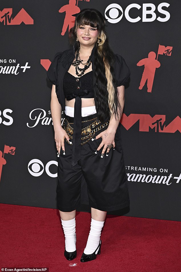 Singer Lola Young was seen in a black crop to, jacket, and capri pants. She accessorized with a slew of gold belts, chunky necklaces, and high socks, and there was way too much going on