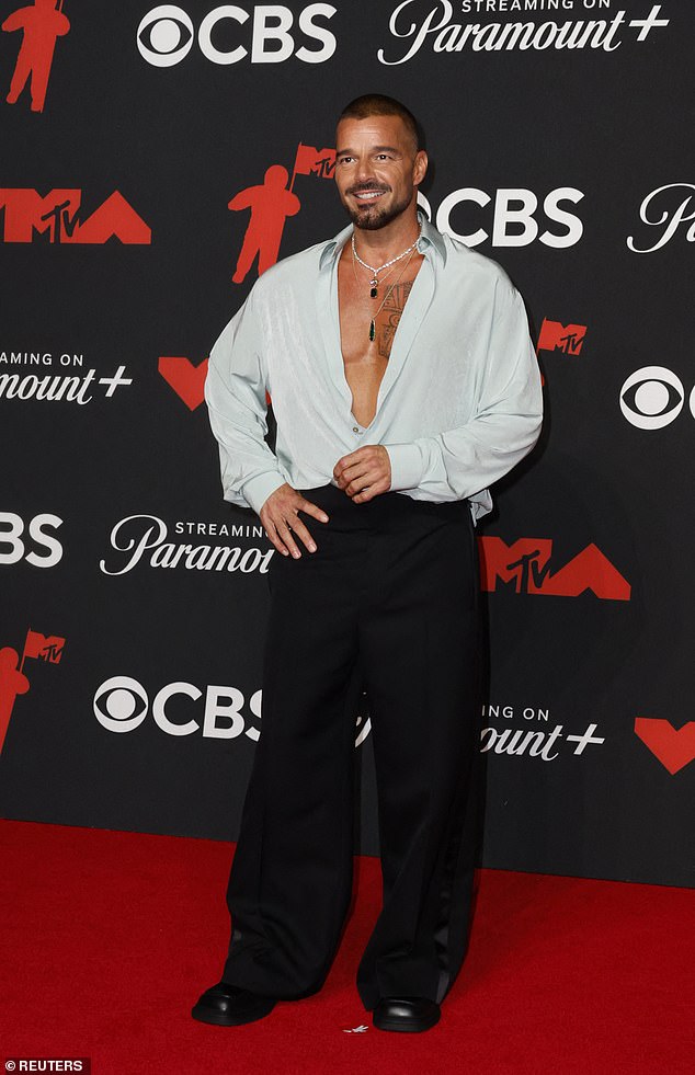 Ricky Martin, 53, wore a halfway unbuttoned blue silk shirt with oversized black pants