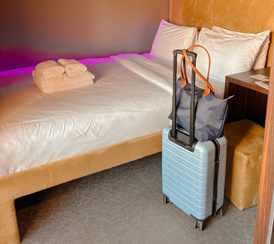 Small hotel room with a bed, luggage, and towels.