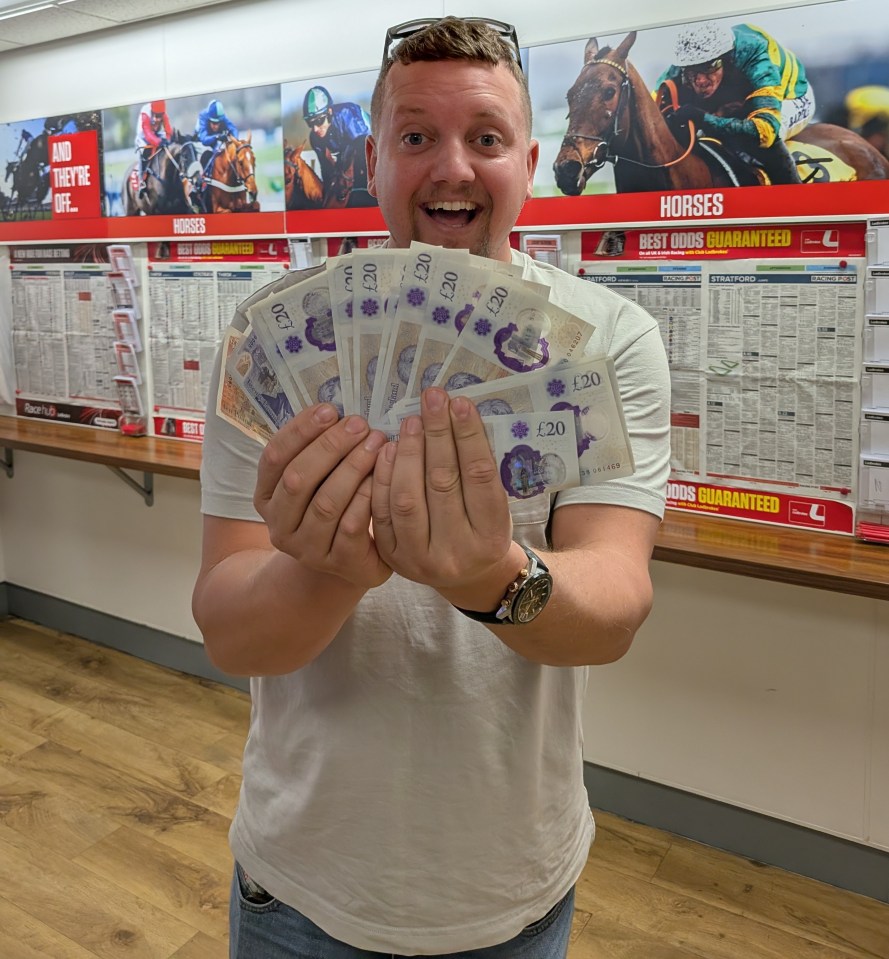 Man holding a fan of twenty-pound notes, smiling.