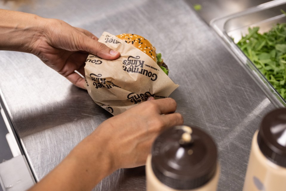 Hands wrapping a Burger King Gourmet Kings burger in branded paper.