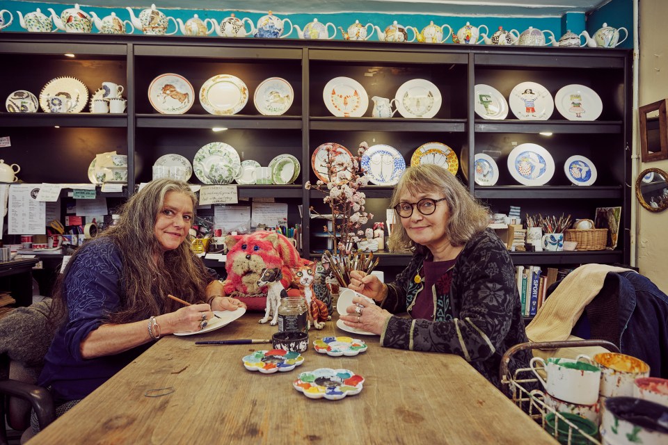 Two women painting bone china in a pottery shop.
