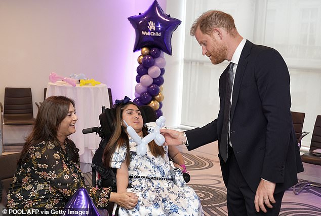 The Duke of Sussex plays with a modelling balloon with previous award recipient Rhea Talwar and her mother Purabi at the annual WellChild Awards