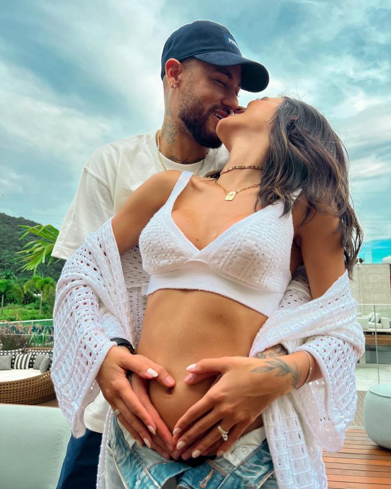 Bruna Biancardi and Neymar Jr. embracing, hands forming a heart over her pregnant belly.
