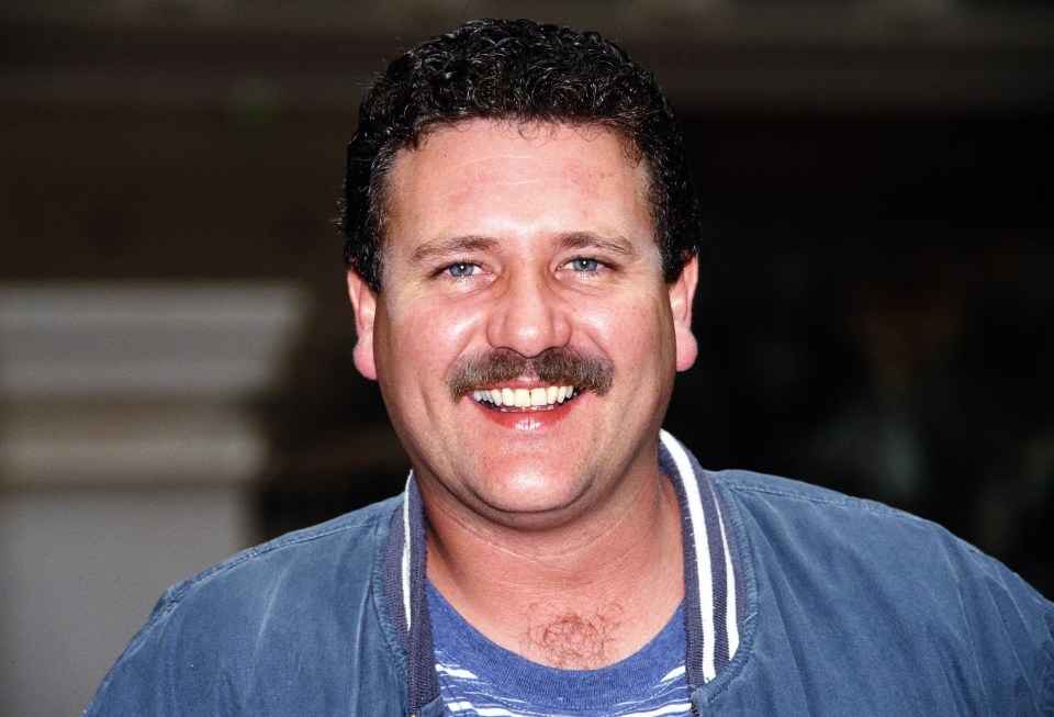 a man with a mustache is smiling and wearing a blue jacket